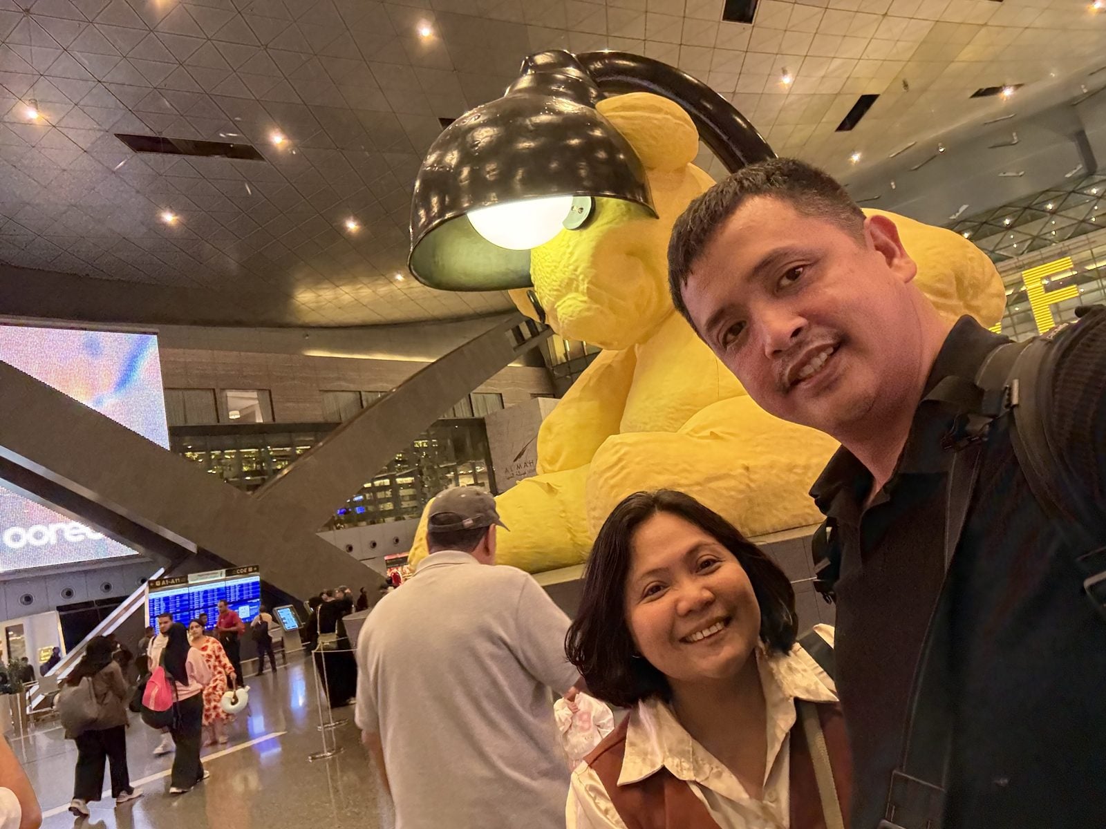Paolo and Rosed selfie with the Lamp Bear at Hamad International Airport, Doha