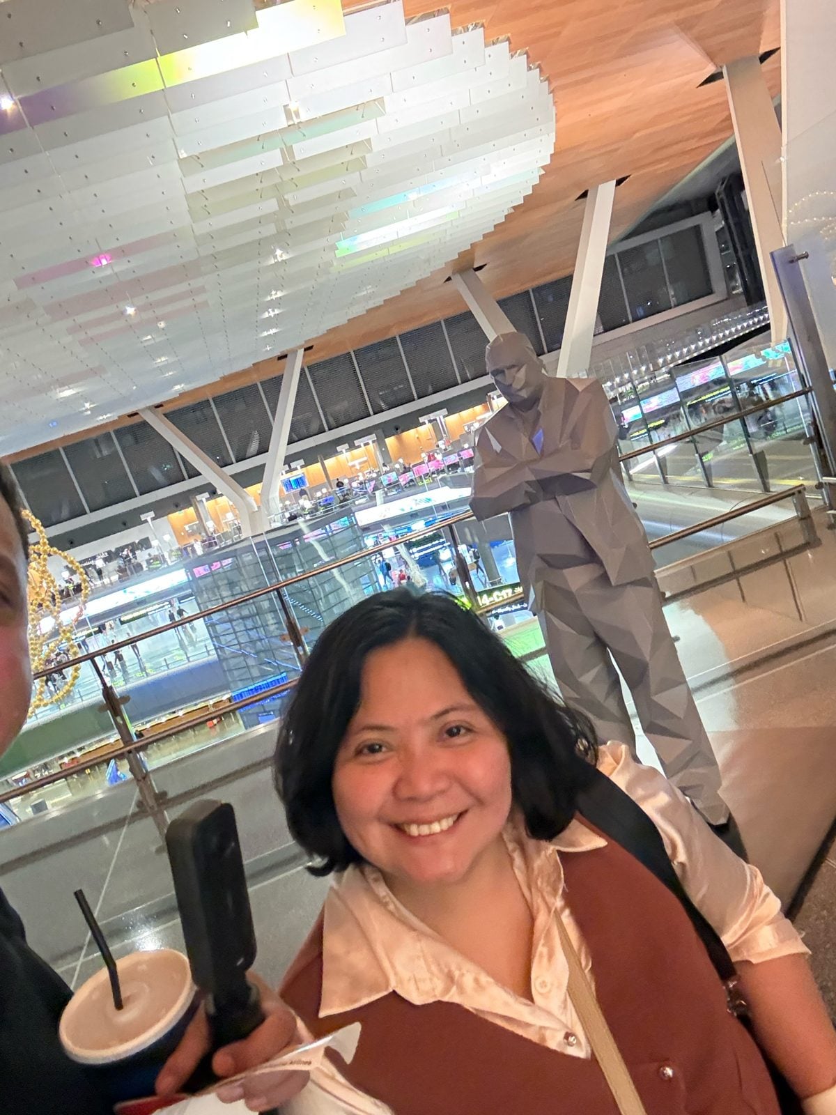 Paolo and Rosed selfie by the grey low-poly statue at Hamad International Airport, Doha