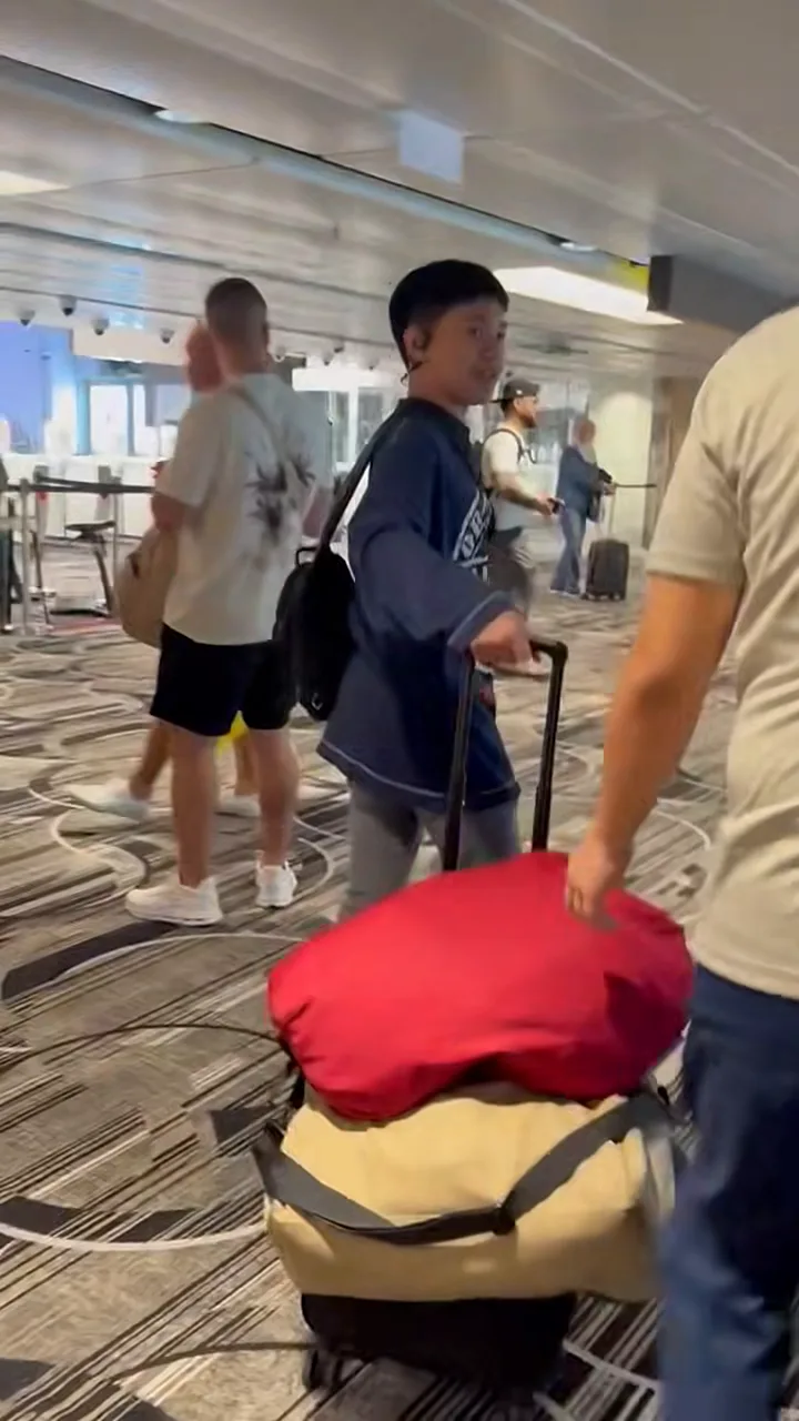 Boy pulling a suitcase piled with red and beige bags through Changi Airport after landing in Singapore