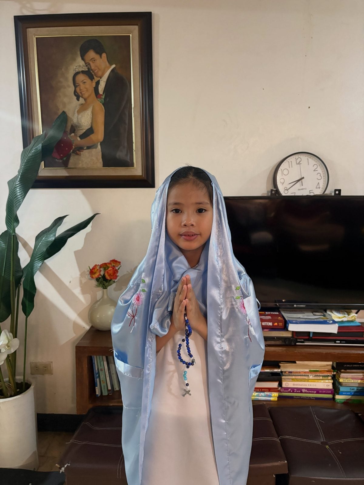 Chloe dressed as Mama Mary in a light-blue veil, holding a rosary
