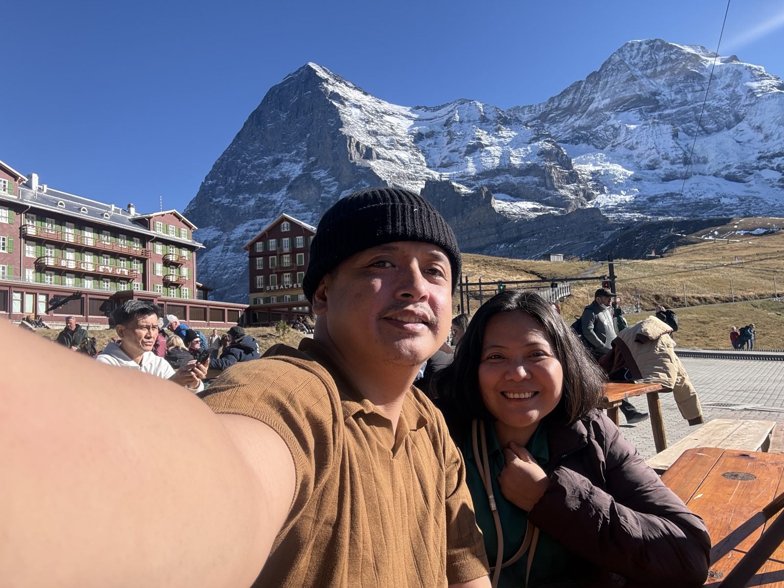 Paolo and Dimple at the outdoor tables at Kleine Scheidegg, with the Eiger and the Bellevue des Alpes hotel