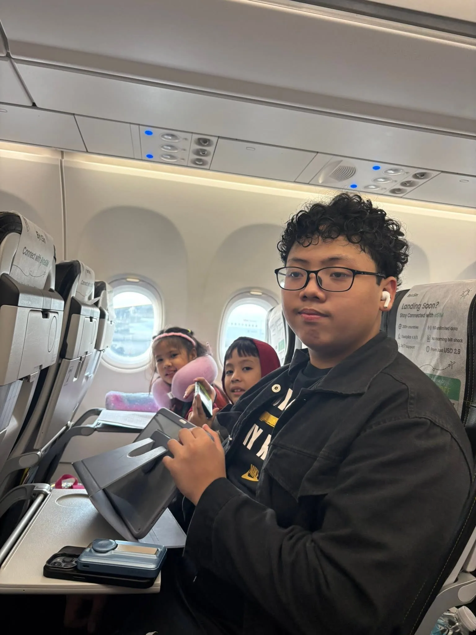 Boy in glasses waving from his plane seat on the flight from Manila to Singapore