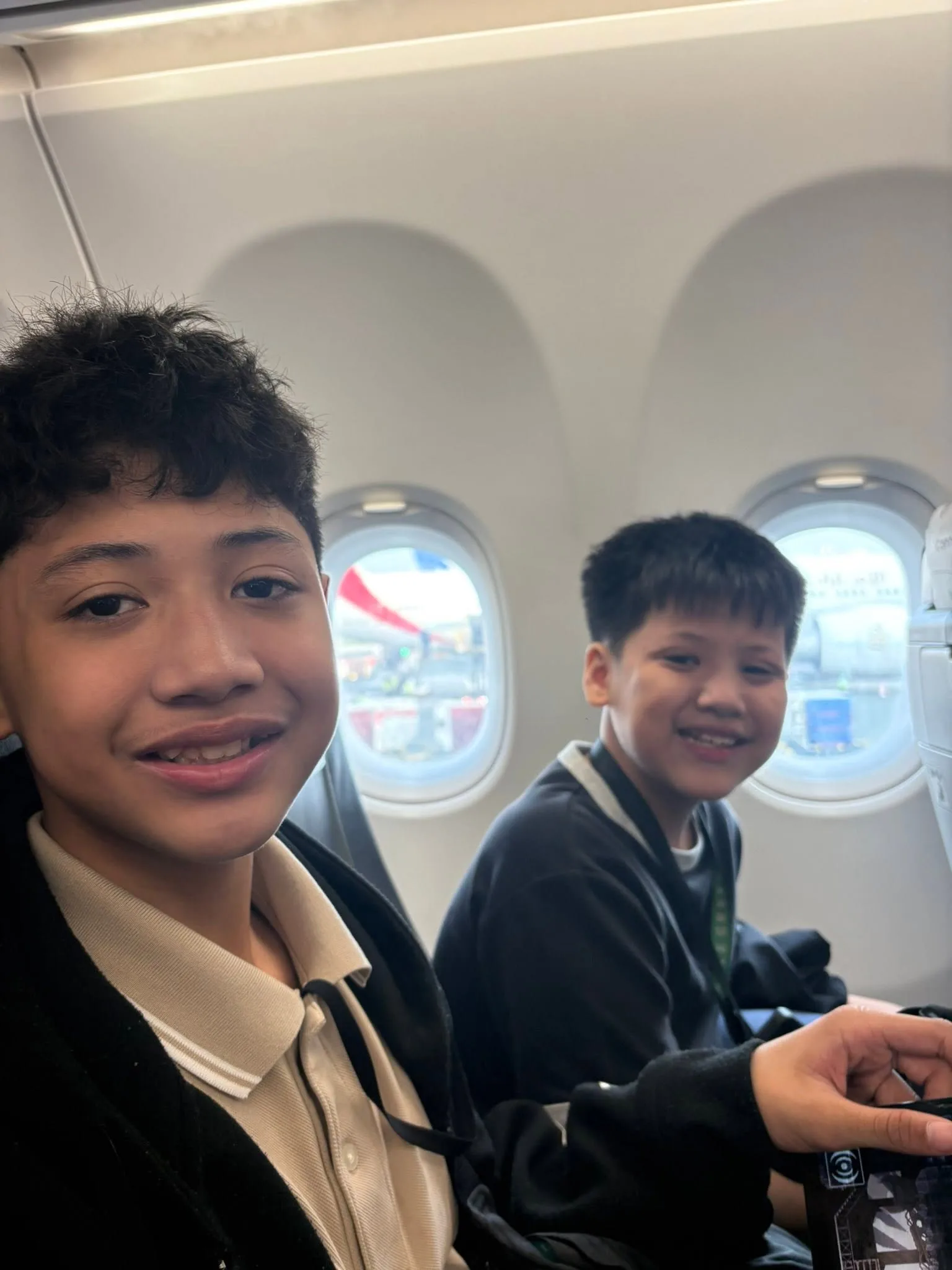 Two boys smiling by the plane window on the flight to Singapore