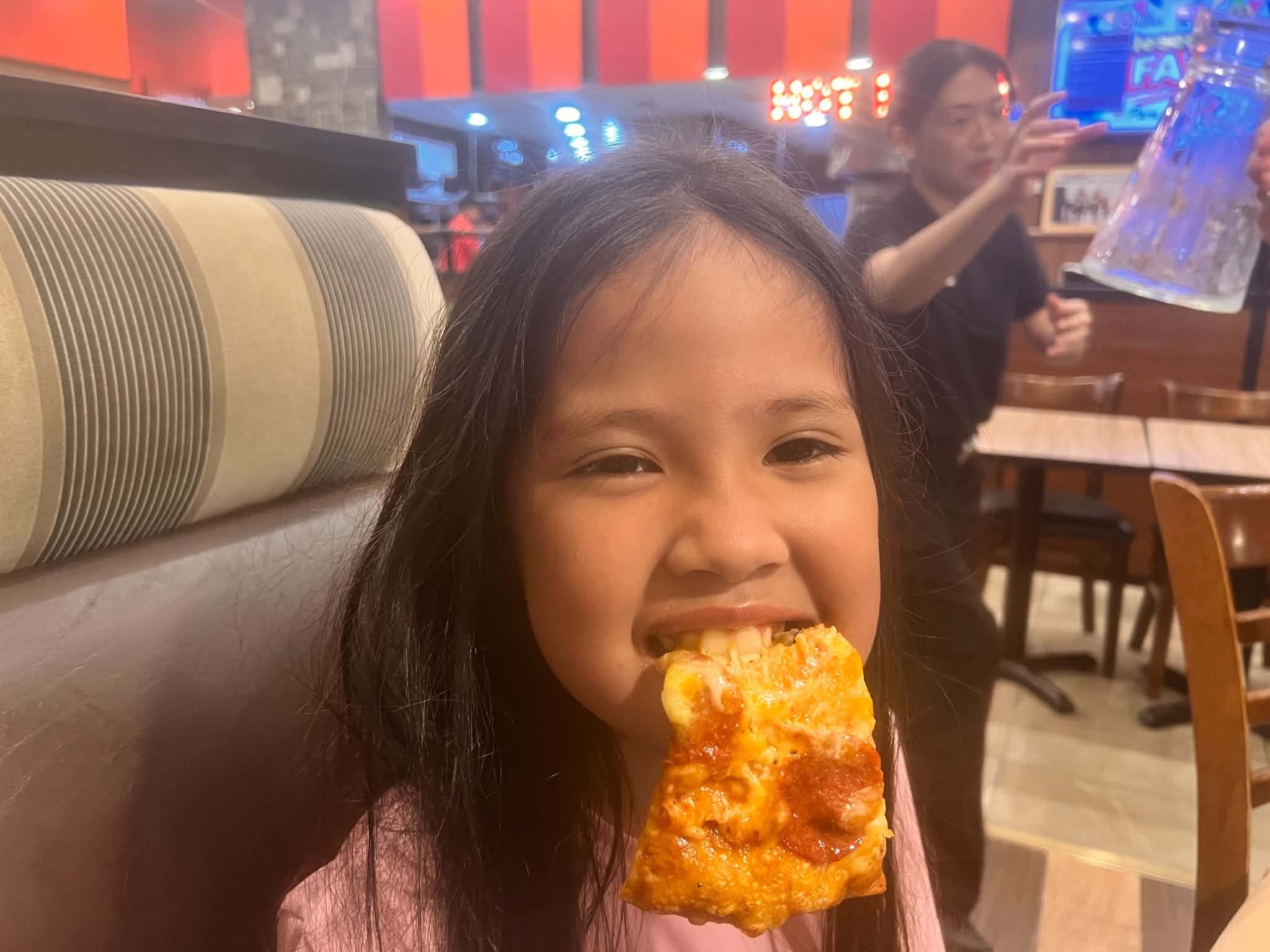 Chloe taking a big bite of Shakey's pepperoni pizza, all smiles
