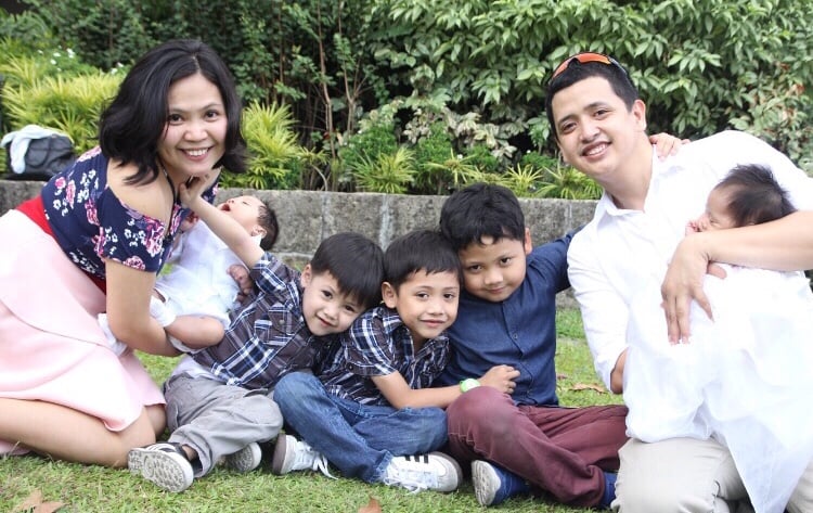 Paolo and Dimple each holding one of the twins in white, sitting on the grass with three boys in between them