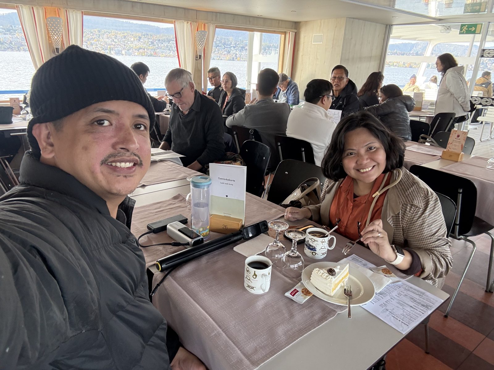 Paolo and Dimple at a window table on a Lake Zurich cruise boat with coffee and a slice of vacherin ice cream cake