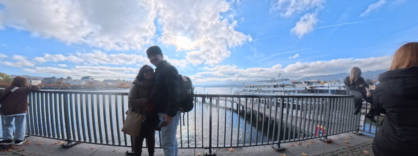 Panorama of Paolo and Dimple at the Lake Zurich railing with a cruise boat behind