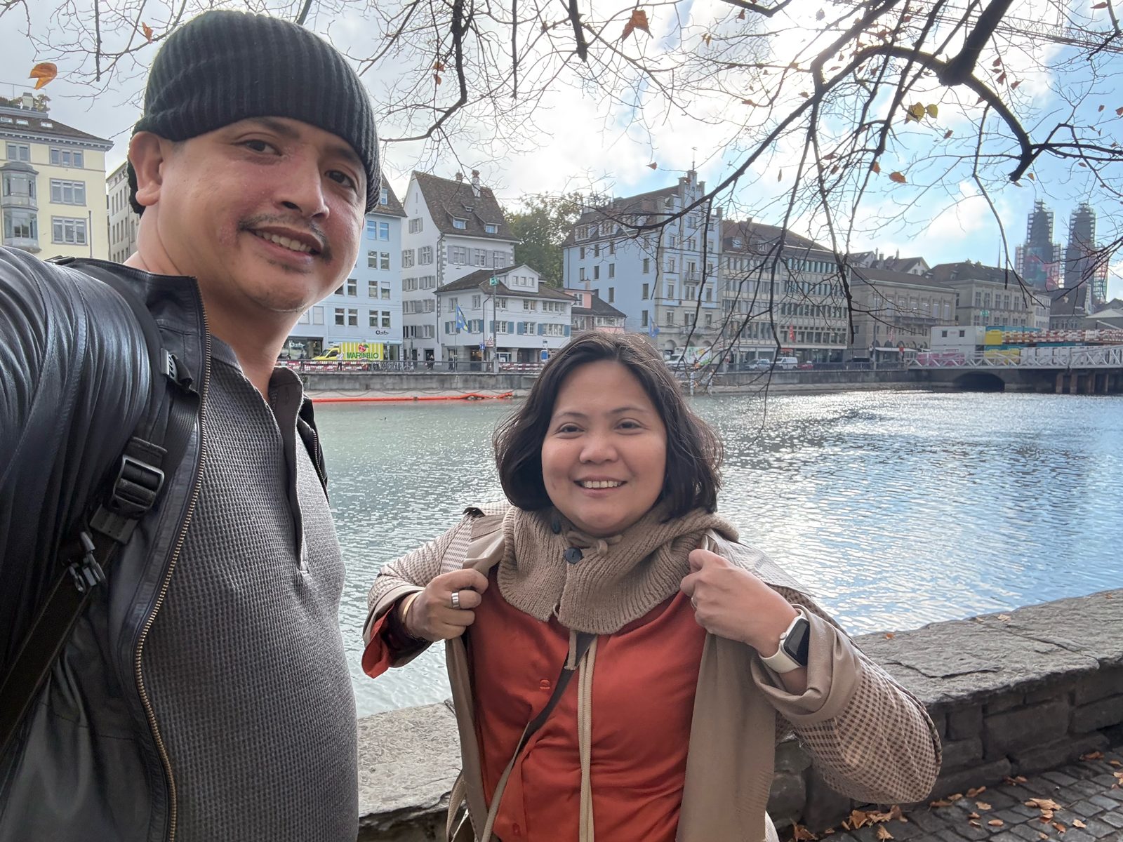Paolo and Dimple on the Limmat riverside with the Grossmünster towers in the distance