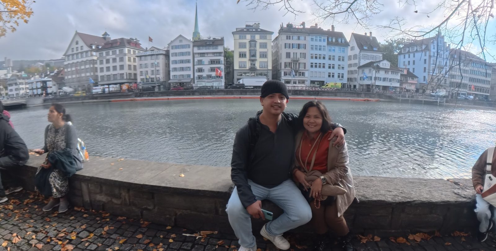 Paolo and Dimple sitting on the stone wall along the Limmat in Zurich Old Town